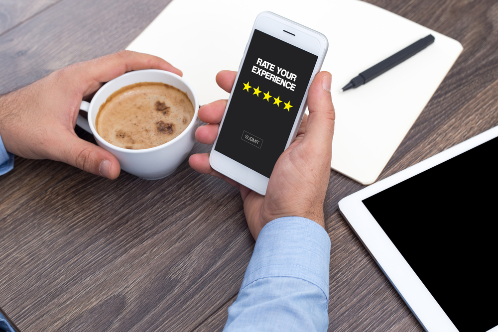 person holding coffee cup in one hand and mobile in another with "rate your experience" written on screen